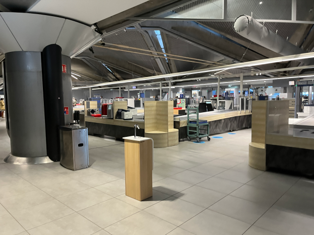 Ein geräumiger Raum im neuen Terminal des Frankfurter Flughafens, gefüllt mit Tischen, Stühlen, Säulen und verschiedenen Gegenständen, mit einigen Menschen und der Decke sichtbar.