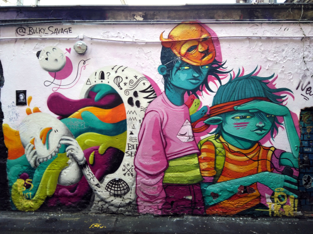 Mural an einer Gebäudeseite mit Graffiti, das eine Straße am Boden, Strommasten und einen klaren blauen Himmel im Hintergrund zeigt.