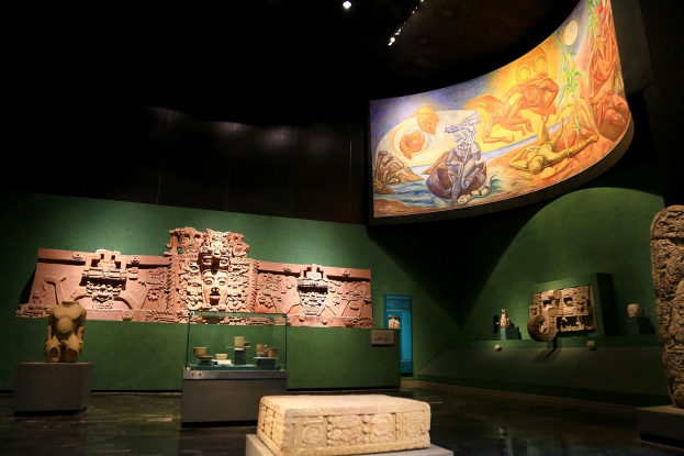 Ein Museumsraum mit verschiedenen Artefakten, darunter Skulpturen, Tischgegenstände, eine Texttafel, eine Wandmalerei und Deckenleuchten im Mexiko-Stadt-Museum der Anthropologie.