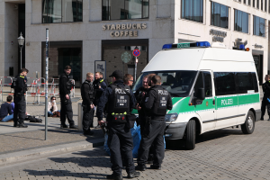 Eine Gruppe von Polizeibeamten steht vor einem Starbucks-Café, mit einem Van auf der rechten Seite und einigen Menschen auf der linken Seite und einem Gebäude mit Fenstern, einem Schild, einem Laternenpfahl und einem Zaun im Hintergrund.