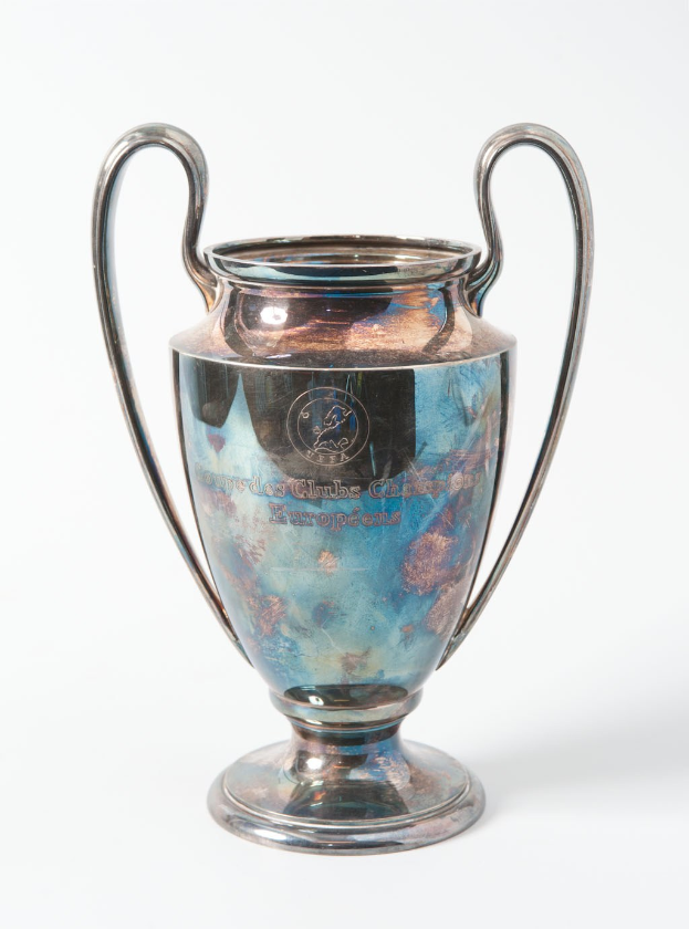 Der UEFA-Champions-League-Pokal, ein stählerner Becher mit zwei Griffen und einem blauen und silbernen Farbschema, mit der Inschrift "UEFA Champions League", gegen einen weißen Hintergrund dargestellt.