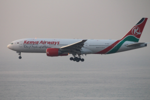 Airbus A330-300 von Kenya Airways im Flug mit weißer, roter und grüner Lackierung vor einem blauen Himmel und glitzerndem Wasser darunter.