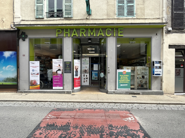 Apotheke mit Glasw├Ąnden und -türen, Plakate an den W├Ąnden, an einer Straßenecke gelegen.