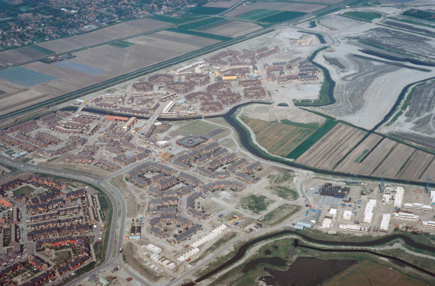 Luftaufnahme einer Stadt mit dichtem Gebäudebestand, Straßen, Grünflächen, Bäumen und einem zentralen Reservoir, das von städtischen Gebieten umgeben ist.