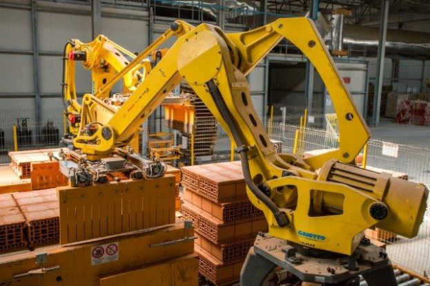 Großes industrielles Lager mit gestapelten Kisten, Kränen an der Decke, Zaun, Pfählen und einer fernen Wand in einer automatisierten Fertigungsumgebung.