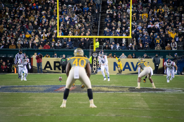 Fußballspieler in Sportbekleidung und Helmen auf einem Feld mit Zuschauern auf den Rängen und Stadionwerbung im Hintergrund.