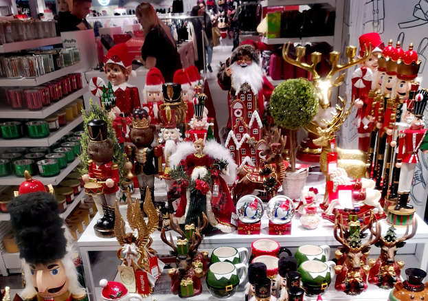 Ladeninneres mit Weihnachtsartikeln wie Spielzeug, Tassen und anderen Gegenständen auf Tischen und Regalen dekoriert, mit Menschen, Lichtern und einer Wand im Hintergrund.