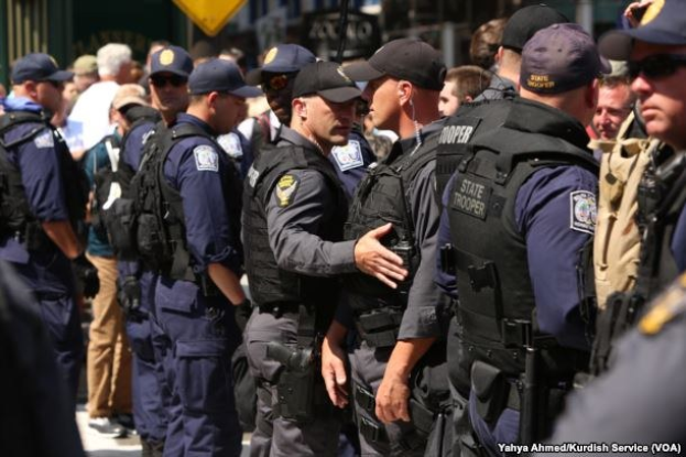 Eine Gruppe von Polizisten in Uniform steht zusammen auf einer Straße, einige halten Waffen, mit Gebäuden und Schildern im Hintergrund.