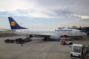 Lufthansa Airbus A320-200 auf dem Frankfurt Airport mit Bodenfahrzeugen, Verkehrskegeln und Informationsschildern im Hintergrund bei bewölktem Himmel.