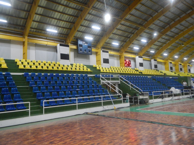 Innenhalle mit Holzboden, blauen und gelben Sitzplätzen, Geländern, Treppen, wandmontierten Bildschirmen, Deckenleuchten und einigen Personen.