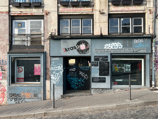 Ein Gebäude mit Fenstern, Geländern, Türen, Texttafeln, Plakaten, Pfählen und Graffiti neben einer Straße.