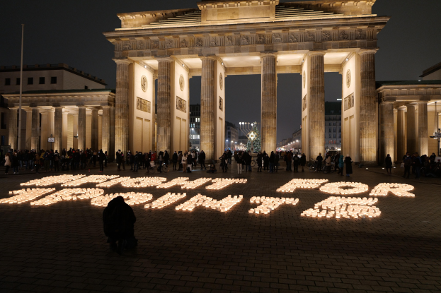Eine Gruppe von Menschen steht vor dem beleuchteten Brandenburger Tor in Berlin, Deutschland, umgeben von Geb├Ąuden und Laternen. Die Worte "K├Ąmpfe für die Freiheit" sind im Vordergrund zu sehen.