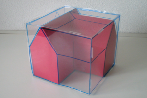 Eine pink-blaue Wahlurne mit offenem Deckel auf einem weißen Tisch vor einer Wand.