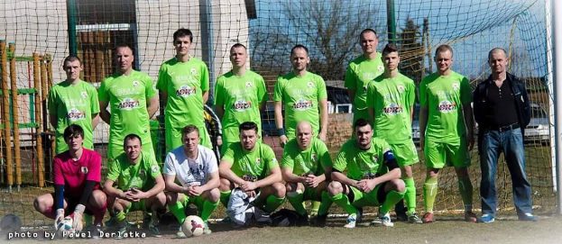 Eine Gruppe von Männern in grünen T-Shirts steht auf einem Fußballfeld, einige hocken, mit einem Ball vor ihnen und einem Torpfosten rechts daneben.