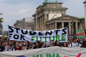 Eine Gruppe von Schülern marschiert in Berlin, eine bunt bemalte 'Students for Future'-Schultafel tragend.
