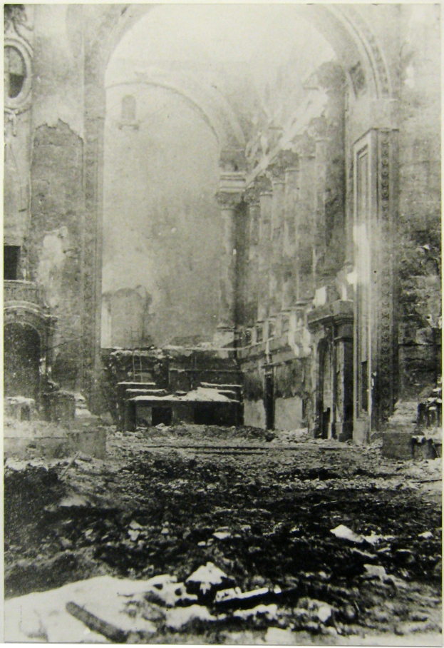 Schwarzes und weißes Foto eines feuerbeschädigten Gebäudes mit Trümmern auf dem Boden und sichtbaren Wänden und Säulen mit Text unten.