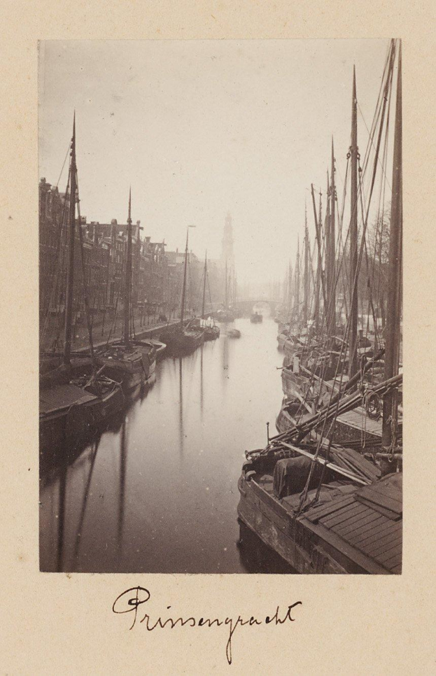 Schwarzes und weißes Foto von Booten in einem Hafen mit Gebäuden auf beiden Seiten und einer Brücke im Hintergrund, mit Text unten.