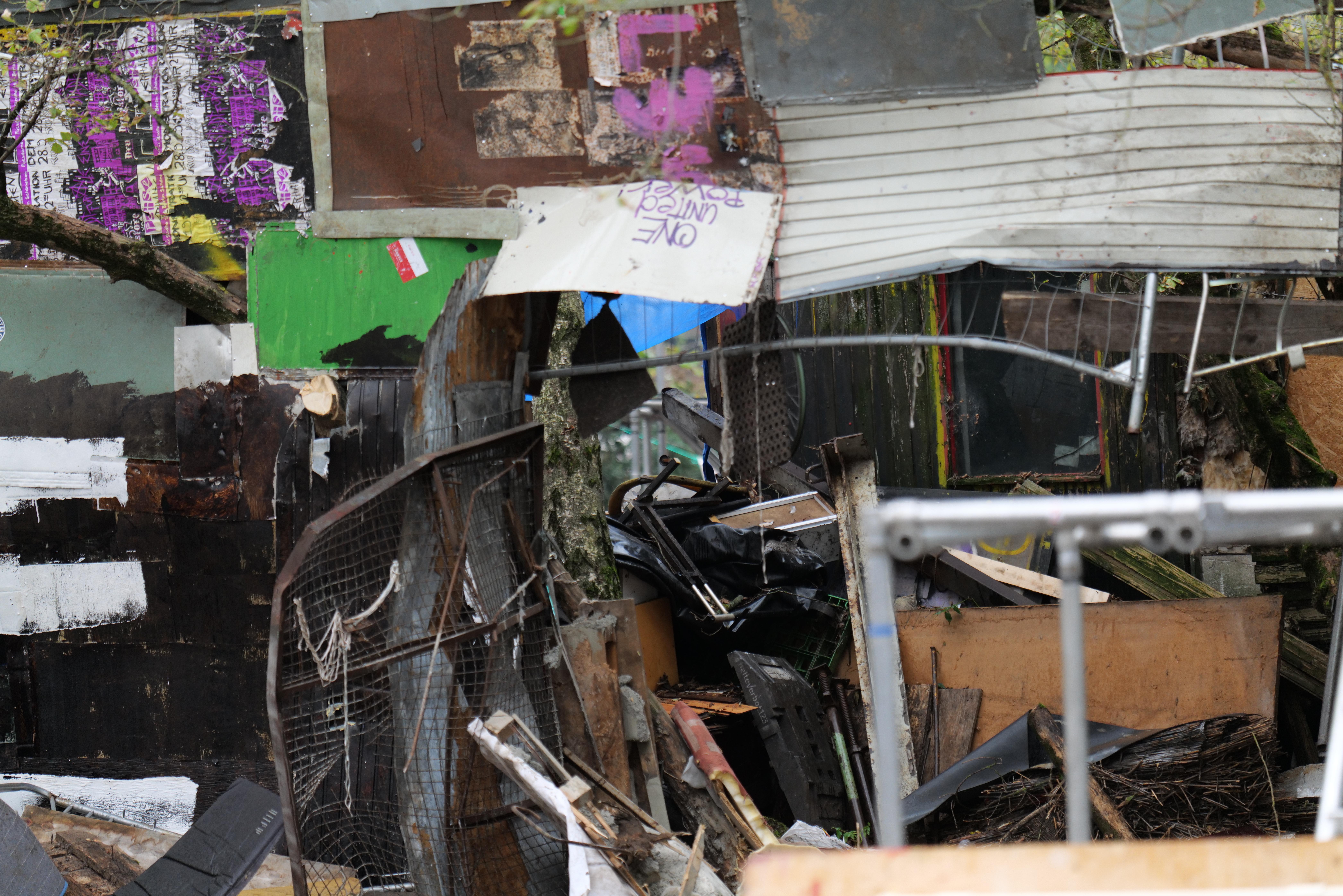 Ein Haufen Müll liegt vor einem mit Graffiti beschmierten Gebäude, umgeben von Bäumen und anderen Gegenständen.