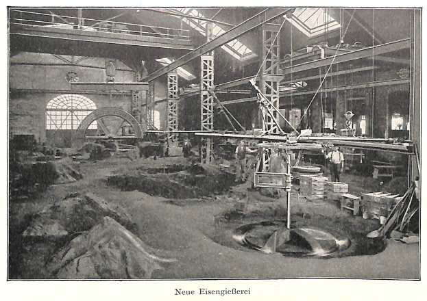 Schwarzes und weißes Foto eines Werks mit Arbeitern, die Maschinen bedienen, umgeben von Metallstangen und -pfählen, beschriftet mit "Neue Eisengießerei, die erste Fabrik in Deutschland."