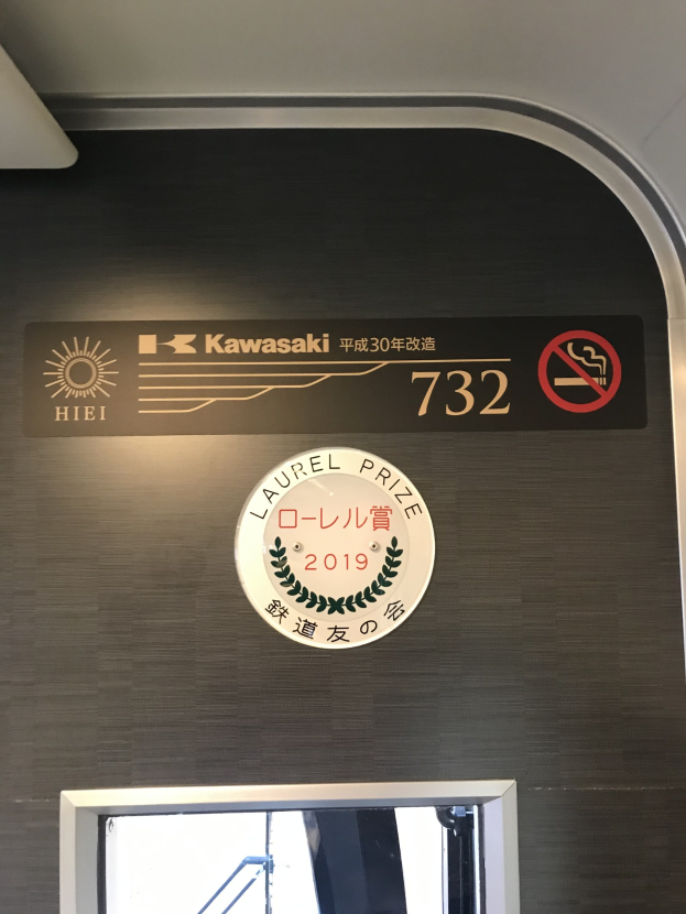Eine Wand mit einem Schild, auf dem "Kawasaki 732" steht, und einem Glasfenster rechts daneben.