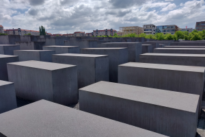 Konkreter Holocaust-Mahnmal für die ermordeten Juden Europas in Berlin, Deutschland, mit Bäumen, Gebäuden und Wolken im Hintergrund.