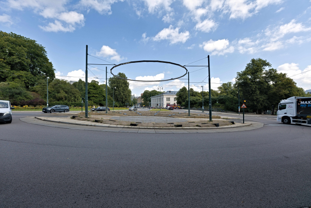 Rundverkehr mit Autos und Lastwagen, umgeben von Pfählen, Bäumen, Gebäuden und einem bewölkten Himmel.