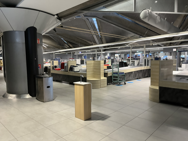 Ein geräumiger Raum im neuen Terminal des Frankfurter Flughafens, gefüllt mit Tischen, Stühlen, Maschinen und Säulen, mit wenigen Menschen und einer sichtbaren Decke.