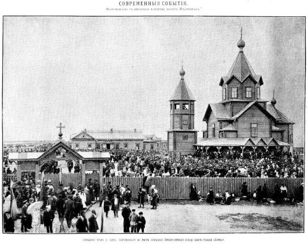 Schwarzes und weißes Foto einer Menschenmenge vor der Kirche der Interzession am Nerl mit einem hölzernen Zaun im Vordergrund und Gebäuden im Hintergrund.