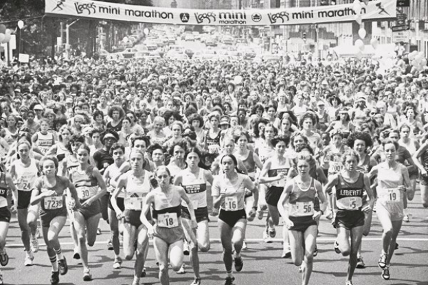 Eine Gruppe von Läufern bei einem Marathon, mit Zuschauern an der Straße, unter einem Banner mit Text, in einem Schwarz-Weiß-Bild.