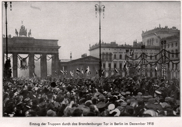 Große Menschenmenge mit Hüten und einigen Fahnen vor dem Brandenburger Tor in Berlin, Deutschland, 1918, mit den Säulen und Statuen des Tors im Hintergrund.