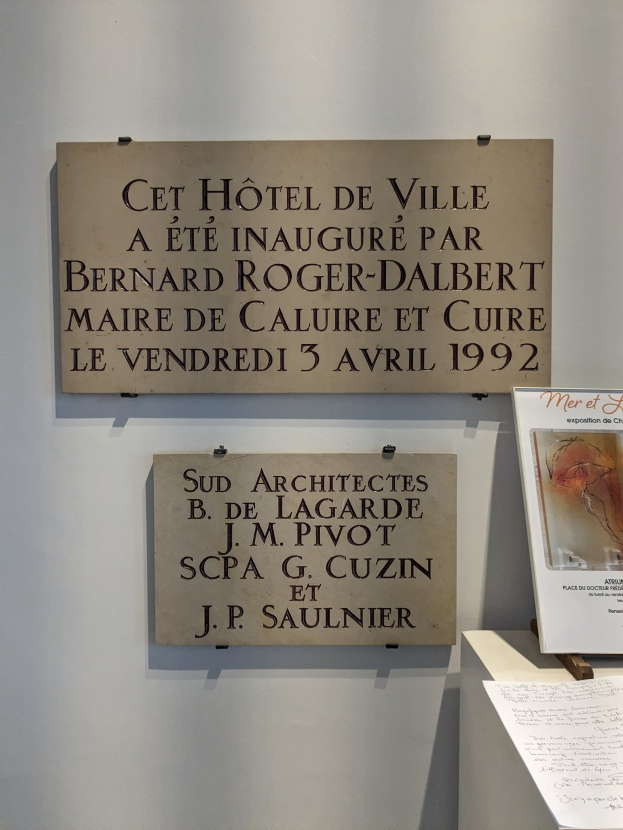 Eine Wandtafel mit der Aufschrift "Cet Hotel de Ville" neben einem aufgestellten Rahmenfoto.
