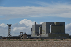 Ein Kernkraftwerk auf einem Feld, umgeben von Gebäuden, Türmen und Pflanzen, mit einer bewölkten Himmel im Hintergrund.