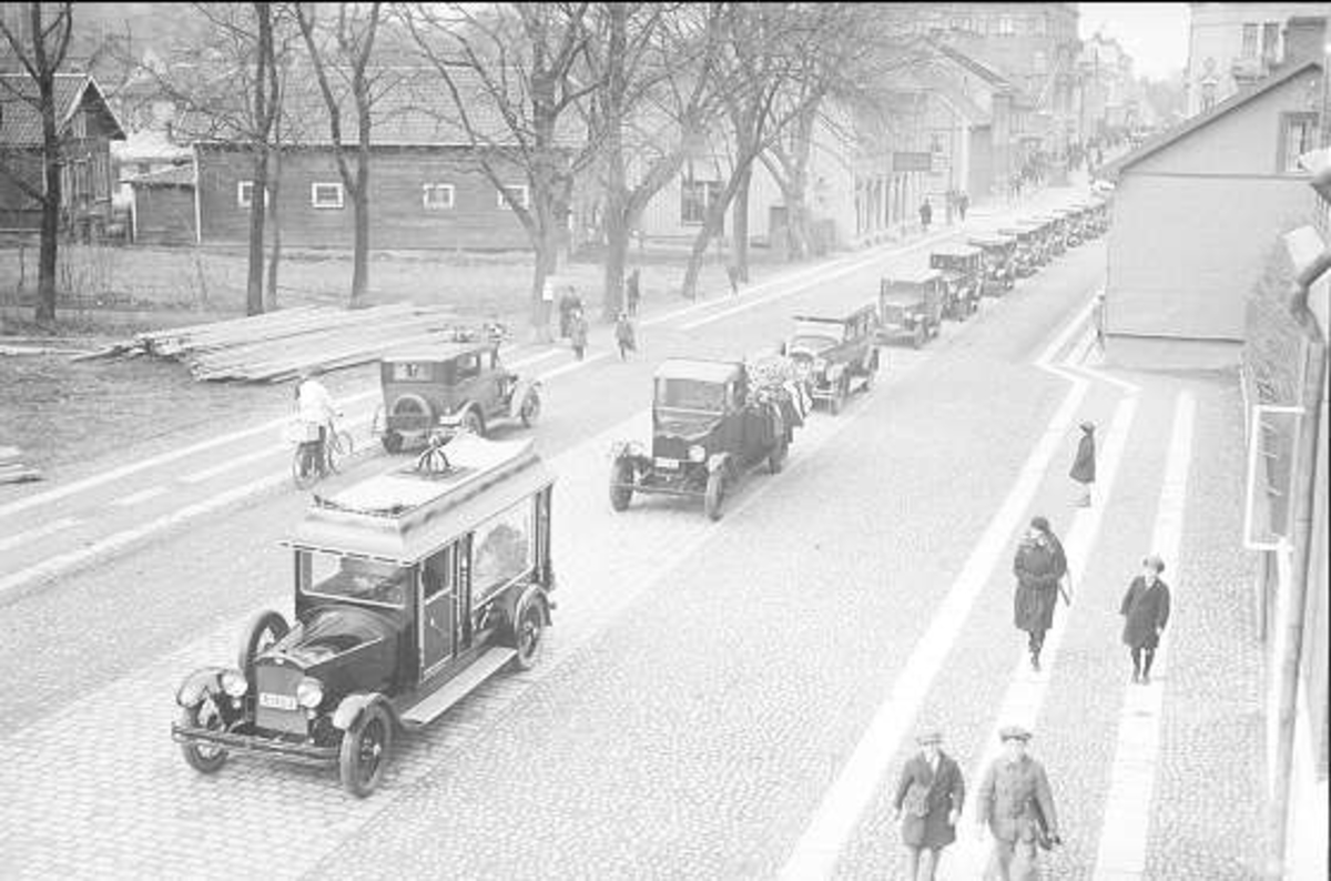 Ein Schwarz-Weiß-Foto einer belebten Straße in Berlin aus den 1930er-1940er Jahren, das Autos, Passanten, Gebäude mit Fenstern, Bäume und einen klaren Himmel zeigt, mit dem Text '1930er-1940er Jahre deutsche Autos in Berlin' unten.