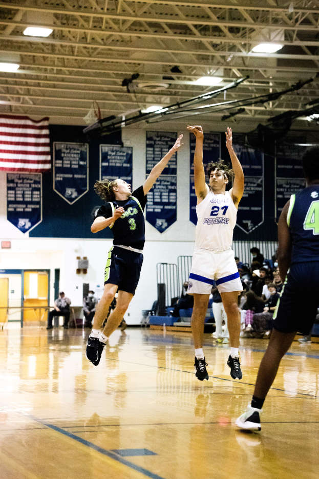 Eine Gruppe von Menschen, die Basketball in einer Turnhalle spielt, mit Zuschauern im Hintergrund, Bannern und einer Flagge an der Wand und einer Decke mit Stangen und Lampen oben.