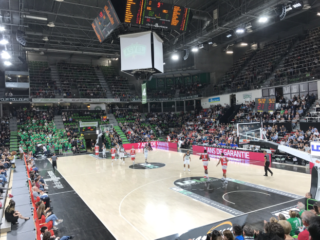 Basketballspiel zwischen Asvel und Galatasaray in einem vollen Hallenstadion mit Anzeigetafeln und Deckenbeleuchtung.