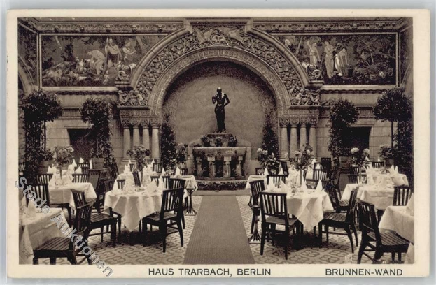 Schwarz-weiß-Foto eines alten Berliner Restaurant-Interieurs mit Tischen, Stühlen, Blumenvasen, einer Statue im Hintergrund, Wandskulpturen, Pflanzen und Text unten.