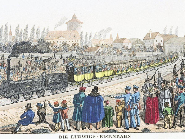 Eine Gruppe von Menschen, die um einen Zug auf einem Gleis herumstehen, einige sitzen im Zug und andere stehen draußen, in der Nähe von Gebäuden und Bäumen, mit dem Text "Ludwigs-Eisenbahn, die erste Bahnstation in Deutschland" unten.
