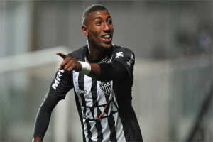 Fußballspieler in schwarzem und weißem gestreiftem T-Shirt, der ein Tor feiert und lächelt, Hintergrund unscharf.