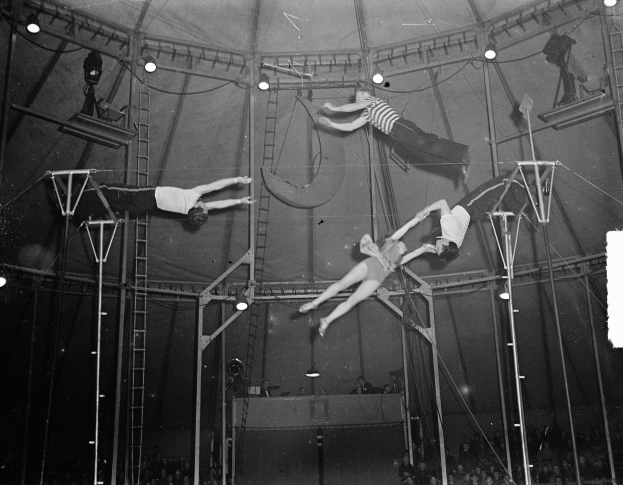 Schwarzes und weißes Foto von Akrobaten, die in einem Zirkuszelt vor einem Publikum auftreten.