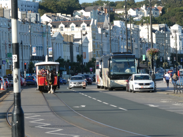 Vollständige Stadtstraße mit hohen Gebäuden, Fahrzeugen, Füpfen, Verkehrsampeln, Laternenmasten, Schildern, Bäumen und einem klaren blauen Himmel.