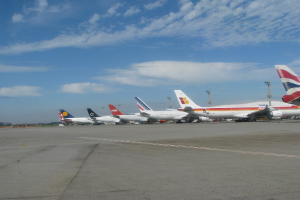Mehrere Flugzeuge stehen auf der Rollbahn mit Polen und Kabeln in der Nähe, unter einem bewölkten Himmel.