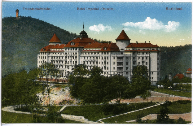 Alte Postkarte des Hotel Imperial in Karlsbad, Deutschland, zeigt ein großes Gebäude mit Fenstern, umgeben von Bäumen, Pflanzen, Gras, einem Weg, einer Baumgruppe, Hügeln und einem bewölkten Himmel, mit Text oben.