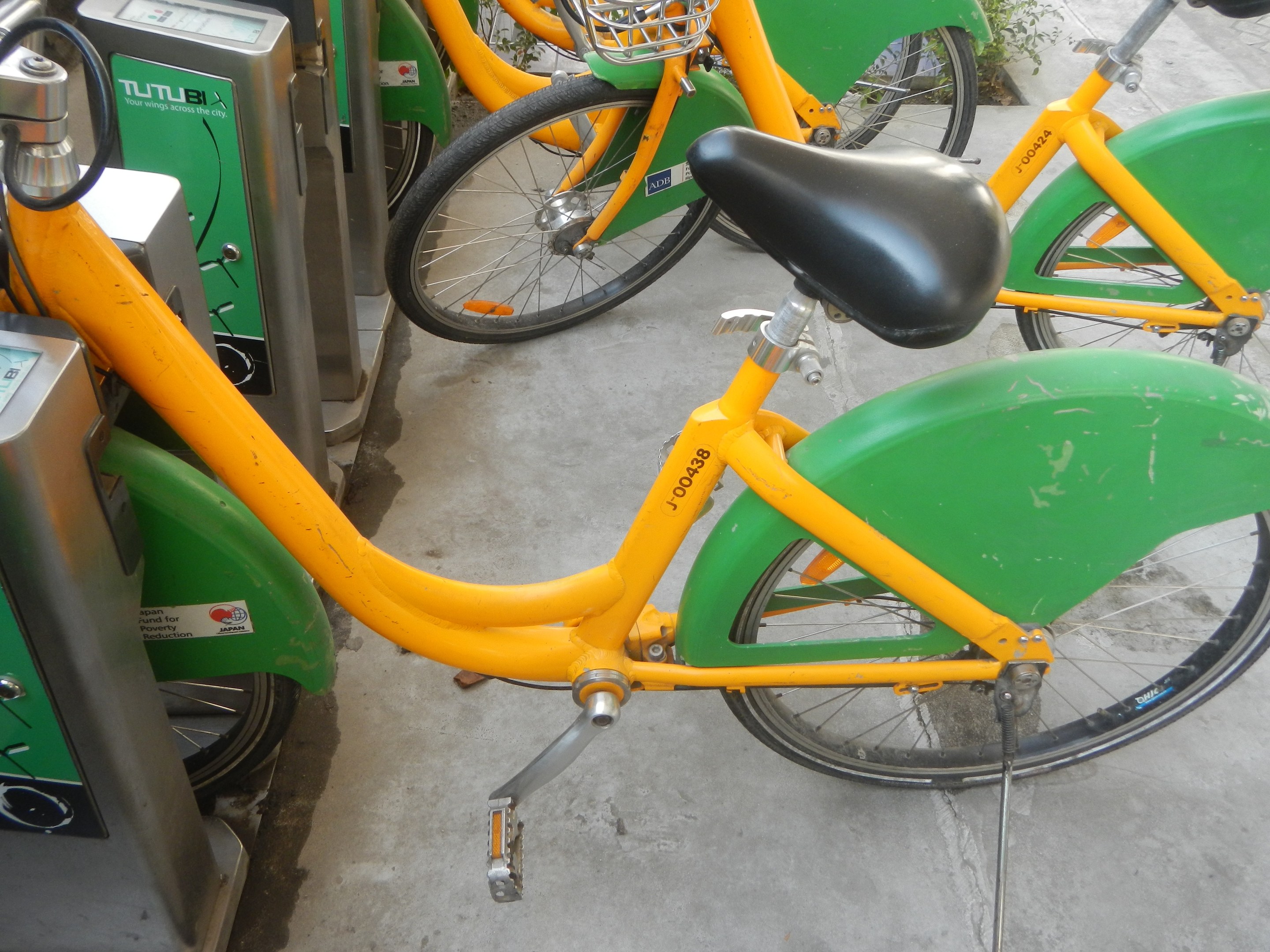 Eine Reihe gelber und grüner Fahrräder nebeneinander geparkt, mit Maschinen links und Pflanzen im Hintergrund.