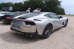 Ein roter Ferrari 812 Superfast ist auf dem Goodwood Festival of Speed geparkt, umgeben von Menschen mit Mützen, Bäumen, Texttafeln und einem bewölkten Himmel im Hintergrund.