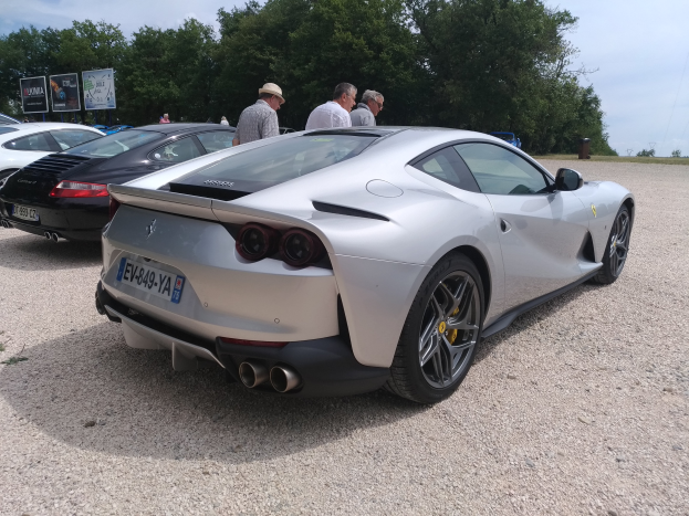 Ein roter Ferrari 812 Superfast ist auf dem Goodwood Festival of Speed geparkt, umgeben von Menschen mit Mützen, Bäumen, Texttafeln und einem bewölkten Himmel im Hintergrund.
