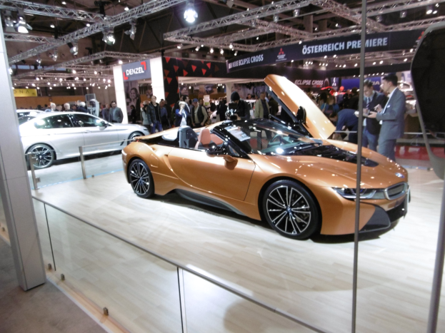 Ein stylischer schwarzer BMW i8 Roadster mit Chromakzenten auf der IAA in Frankfurt umgeben von elegant gekleideten Besuchern in einer Atmosphäre der Aufregung.