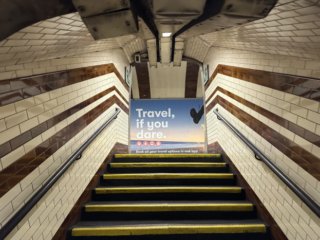 Eine Treppe in einer U-Bahn-Station mit einem 'Reise, wenn du dich traust'-Schild oben, flankiert von Geländern und Stationswänden im Hintergrund.
