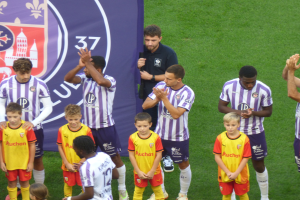 Eine Gruppe junger Jungs auf einem Fußballfeld, die klatschen, mit einem Banner im Hintergrund mit Text und Logos.