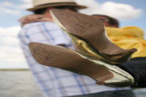 Frau in High Heels mit Aufschrift, Person hält Frau von hinten an den Beinen fest.