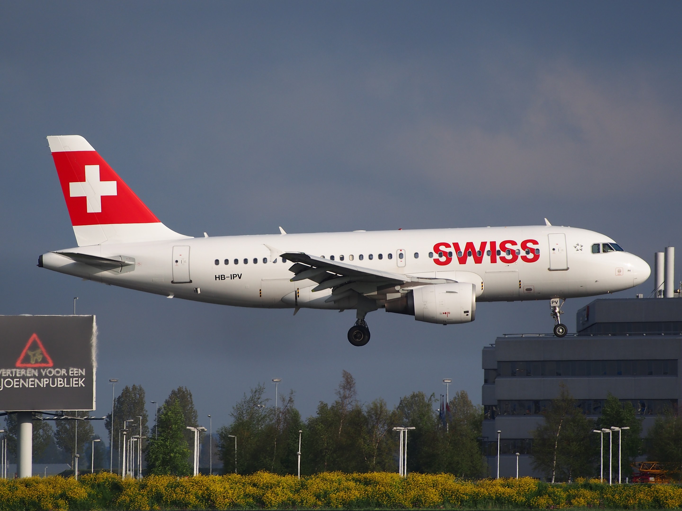 Ein Airbus A320-200 der Swiss International Air Lines startet vom Frankfurter Airport, umgeben von Grünflächen und Infrastruktur, mit einem Schild im Vordergrund und einem bewölkten Himmel.